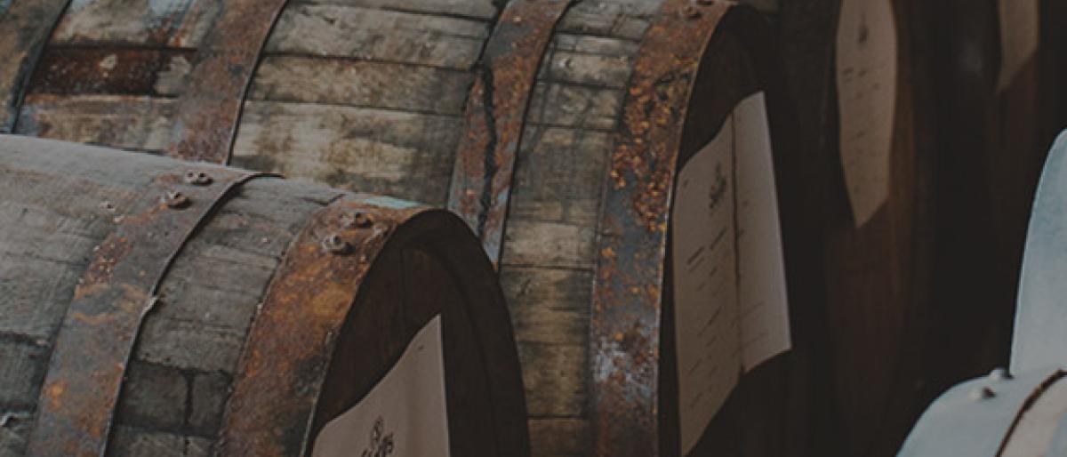 Rows of aged wooden whiskey barrels with white labels stacked in a distillery