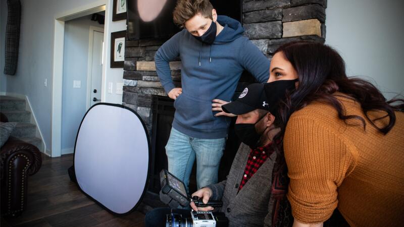 Masked film crew reviewing footage on a camera monitor indoors