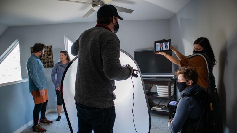 Masked film crew filming with a large reflector in an attic room