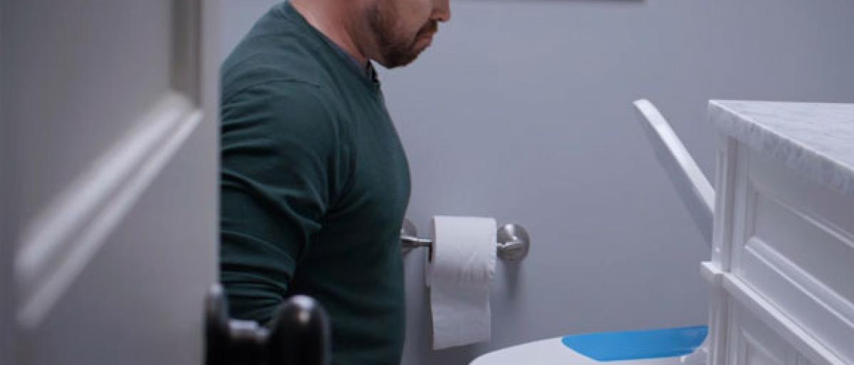 Man beginning to sit on a toilet fitted with a blue-accented Bemis seat
