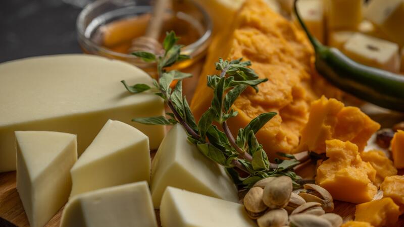 Close-up cheese board with cubed cheddar and Swiss cheese, herbs, honey, and a jalapeno