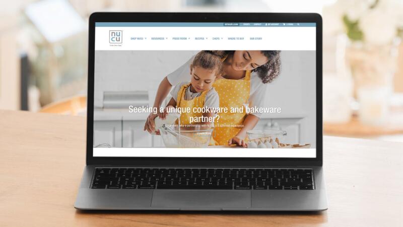Laptop on a table showing the NUCU cookware website homepage with a parent and child baking
