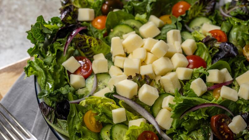 Mixed green salad with cubed cheese, cherry tomatoes, cucumbers, and red onion