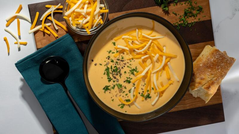 Bowl of cheese soup topped with shredded cheese, herbs, and bread on the side