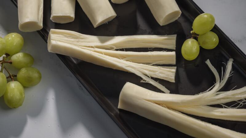 String cheese pulled into strands next to a cluster of green grapes