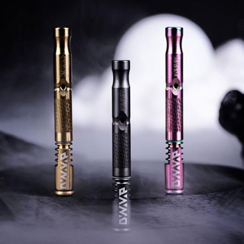 Three DynaVap vaporizer pens in black, gold, and pink finishes against a smoky backdrop