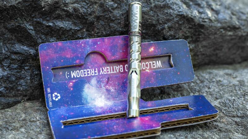 A DynaVap vaporizer pen resting on packaging with a galaxy-print design and battery message
