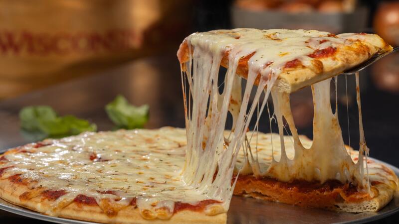 Slice of cheese pizza lifted from the pan with a long cheese pull