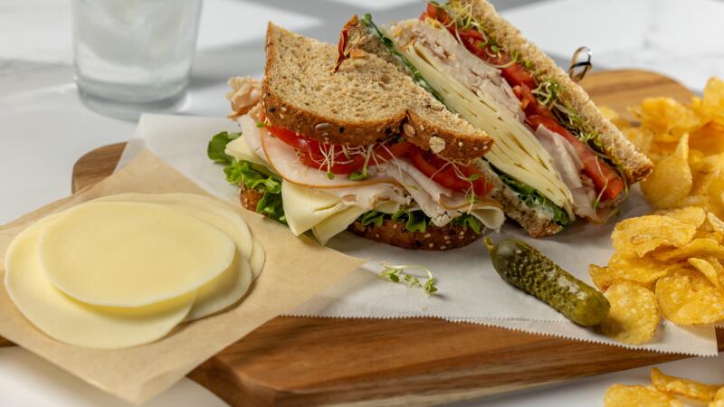 Turkey sandwich with cheese, lettuce, and tomato served with chips and a pickle