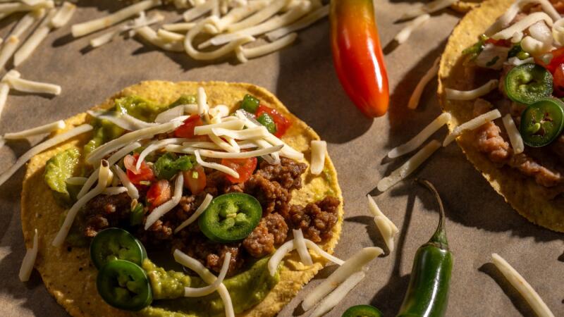 Tostadas topped with shredded cheese, guacamole, seasoned meat, pico de gallo, and jalapenos