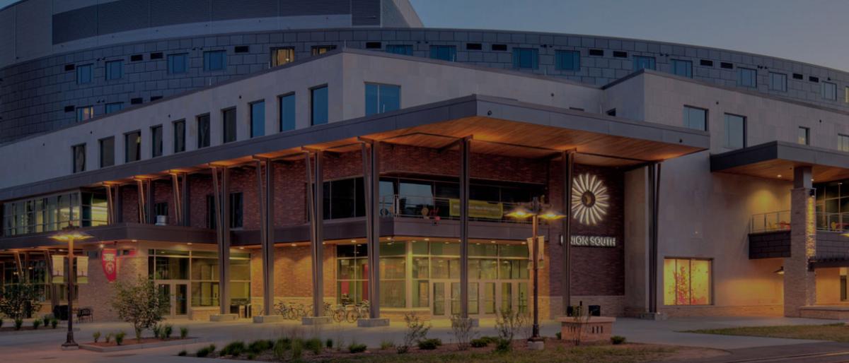 Exterior of the University Union South building at dusk with lit windows and a sunburst logo