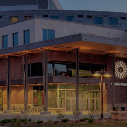 Exterior of the University Union South building at dusk with lit windows and a sunburst logo