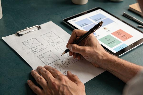 Hand sketching website wireframes on paper next to a tablet